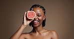 Face of woman, grapefruit and smile in studio for skincare, vitamin c and natural beauty for wellness. Portrait, happy person or dermatology with citrus fruit, skin glow and space on brown background