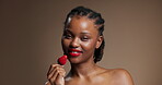 Woman face, eating and strawberry in studio for skincare, natural beauty and vitamin c for wellness glow. Portrait, happy person or dermatology with fruit, brighten skin and space on brown background