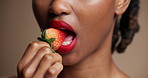 Lipstick, strawberry and mouth of woman in studio for beauty, cosmetics and skincare. Aesthetic, cosmetology and person eating fruit with red lips for gloss, shine and makeup on brown background