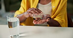 Hands, medication and water with person at desk in living room of home for dosage or treatment. Drink, glass and pills for chronic disease with woman at table in apartment for supplement benefits