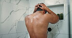 Man, shower and back in home bathroom for cleaning, wellness and washing hair. Male person, house and running water in morning for skincare, splash and fresh body with grooming cosmetics and shampoo
