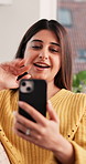 Phone, video call and wave with woman on sofa in living room of home for conversation or greeting. App, connection and hello with happy Indian person in apartment for mobile or virtual communication