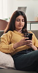 Break, phone and stretching with woman on sofa in living room of home for social media browsing. App, reading text message and relax with Indian person in apartment for communication or me time