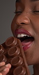 Black woman, skincare and eating chocolate in studio for diet, unhealthy nutrition and sweet treat. Person, beauty cosmetics with candy for calories, cacao dessert and sugar snack on gray background