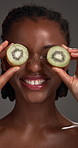 Skincare, kiwi and face of black woman in studio for natural cosmetics, wellness and facial glow. Fruit, dermatology and portrait of person for vitamins, skin hydration and beauty on dark background
