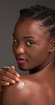 Face, laughing and lotion with black woman in studio to apply moisturizer to shoulder for skincare. Beauty, cream and funny with African model on gray background for cosmetic or dermatology treatment