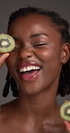 Skincare, kiwi and happy black woman in studio for natural cosmetics, wellness and facial benefits. Fruit, dermatology and face of person for vitamins, skin hydration and beauty on dark background