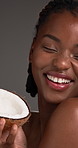 Face, woman and skincare with coconut in studio for beauty, hydration and facial shine. African person, organic and tropical fruit for natural glow, healthy skin and oil treatment on gray background