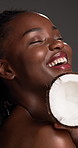 Face, African woman and skincare with coconut in studio for beauty, hydration and facial healing. Smile, person and tropical fruit with natural glow, healthy skin and oil treatment on gray background