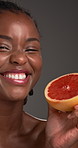 Face, grapefruit and skincare with excited black model in studio for detox or health benefits. Beauty, citrus and vitamin c with funny African woman on gray background for diet, nutrition or wellness