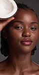 Face, African woman and beauty with coconut in studio for skincare, hydration and facial healing. Smile, person and tropical fruit with natural glow, healthy skin and oil treatment on gray background