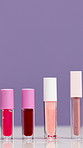 Empty, tube and lip gloss in studio for makeup, cosmetics and product review on purple background. Space, salon and selection of lipstick color for shine, hydration or moisturizer for beauty campaign