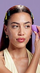 Beauty, makeup and sponge with face of woman in studio for shine, foundation application and self care. Blush powder, aesthetic and highlighter glow with person on purple background for cosmetics