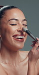 Beauty, laughing and makeup brush with happy woman in studio to apply facial foundation. Contouring, blush and funny with excited model on gray background for application of cosmetic product