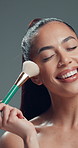 Smile, woman and brush for makeup in studio with beauty, foundation application and aesthetic. Happy, female person and cosmetic tools for makeover, facial powder and natural shine on gray background