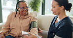 Old woman, caregiver and blood pressure on sofa for talk, assessment or hypertension in retirement. Senior person, medical professional and monitor on couch for healthcare results at nursing home