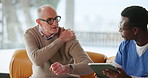 Shoulder pain, tablet and nurse with mature man in home for consulting, medical exam and help. Retirement, sofa and caregiver with person on tech for wellness, online diagnosis and healthcare support