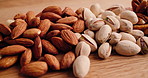 Table, nutrition and many nuts for health, food and natural diet for wellness. Wooden counter, seeds and variety of organic snacks with vegan pecan, almonds or pistachio with benefits closeup