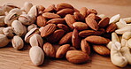 Table, diet and different nuts for health, food and natural nutrition for wellness. Wooden counter, seeds and variety of organic snacks with vegan pecan, almond or pistachio with benefits closeup