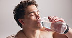 Athlete, man and drinking water for fitness in studio for hydration, refreshing and exercise break. Tired, person and bottle with liquid for training recovery, mineral beverage and white background