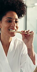 Woman, brushing teeth and mirror in bathroom with reflection for cleaning mouth in morning. African person, toothbrush and oral hygiene for dental care routine, wellness or plaque removal in house