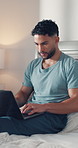 Laptop, typing and man in bedroom as freelancer, editing newsletter and content writing. Computer, remote work and copywriter on bed in home for reading article, blog and research information online
