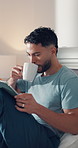 Coffee, ebook and tablet with man in bedroom of home for me time, morning break or wellness. App, caffeine and reading with person drinking beverage on bed in apartment for hobby, literature or story