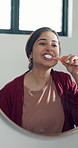 Bathroom, woman and brushing teeth by mirror for health, dental hygiene and oral wellness. Reflection, toothbrush and person cleaning mouth for fresh breath, gum care and morning routine in home