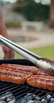 Hotdog, grill and hands of person outdoor for cooking, celebration and barbecue. Meat, bbq lunch and party event with man and sausage in backyard of home for cookout, feast and weekend break