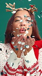 Face, woman and confetti on Christmas in studio for celebration, holiday spirit and fun tradition. Portrait, person and blow glitter for festive, xmas party and sparkle decoration on green background