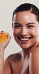 Woman, skincare and squeeze orange at face with smile, natural treatment or vitamin C in studio. Person, citrus fruit or splash on white background for organic care, healthy skin or antioxidants