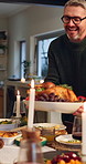 Happy man, turkey and serving meal with family at dinner table for food, dining or thanksgiving. Mature, male person and chicken platter with candle light for hospitality, supper or reunion in home