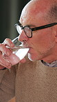 Thinking, senior man and drinking water at house for hydration, refreshing and mineral nutrition. Elderly person, relax and glass with liquid, prevent dehydration and beverage for wellness benefits