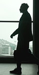 Businessman, silhouette and walking with window in confidence for corporate journey or travel. Male person, employee or traveler with bag in city building for company trip or career opportunity