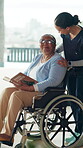 Caregiver, wheelchair and senior women reading book in assisted living facility, support and talking. Retirement, nurse or elderly person with disability in rehabilitation center, comfort and helping