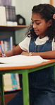 Girl, student and writing with book in library for homework, education or learning in school. Child, kid or learner taking notes with assessment for test, exam or childhood development in study