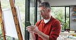 Artist, man and phone in home for art, inspiration or design process for project in lounge. Internet, typing and mature painter with talent for hobby, illustration or creative sketch with craft