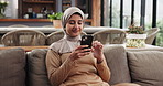 Happy, muslim woman and scroll on sofa with phone for social media, online news or religious guidance. Islamic person, smile or tech in home for browsing mobile app, internet search or entertainment.