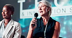 Mature woman, stage and talk at convention for tech innovation, insight and presentation at event. Business people, panel discussion and mic for info, speech or announcement with smile at conference