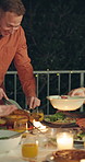 Happy people, night and turkey with serving at outdoor dinner table for thanksgiving meal or gathering. Group, dishing and late evening with plate, chicken or candle light for food or feast together