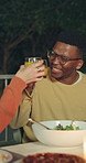 Happy man, night and cheers with juice at dinner table for thanksgiving meal or outdoor gathering. Male person, toast or smile with group of friends, drink or food for feast, reunion or late supper