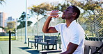 Black man, tennis player and drinking water with bottle on bench for rest, break or recovery. Active, male person or relax with mineral liquid or beverage for sports, hydration or sustainability