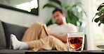 Cup, tea and wellness with man on sofa in living room of home for break, health or me time. Drink, glass and relax with person in apartment for benefits or remedy of herbal beverage and vitamins
