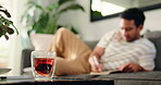 Glass, relax and tea with man on sofa in living room of home for break, health or me time. Cup, drink and wellness with person in apartment for benefits or remedy of herbal beverage and vitamins