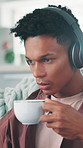 Headphones, coffee and man on sofa in home with listening to music, playlist or podcast for relax. Audio tech, calm and male person drinking warm beverage and streaming album in living room at house.