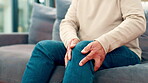 Knee pain, cramps and hands of old man on sofa for osteoporosis, joint injury and inflammation. Arthritis symptoms, fibromyalgia and sprain with legs of person in living room of home for pressure