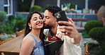 Selfie, kiss and happy couple with flowers at restaurant for love, care and romantic connection. Man, woman and picture on date with bouquet, social media update and post for memory on valentines day
