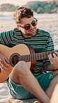 Beach, happy man and playing guitar with sunglasses, summer vacation and holiday for musical interest. Weekend trip, outdoor and musician smile with instrument for melody, ocean and sea for acoustic