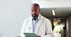 Medical, tablet and walking with doctor black man in hospital for planning or research. App, healthcare and reading with mature African person in clinic hallway for insurance or review of information