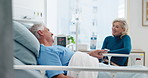 Talking, support and woman with husband in hospital bed for surgery recovery, healing or treatment. Happy, retirement and senior couple with conversation in medical clinic for visit with marriage.